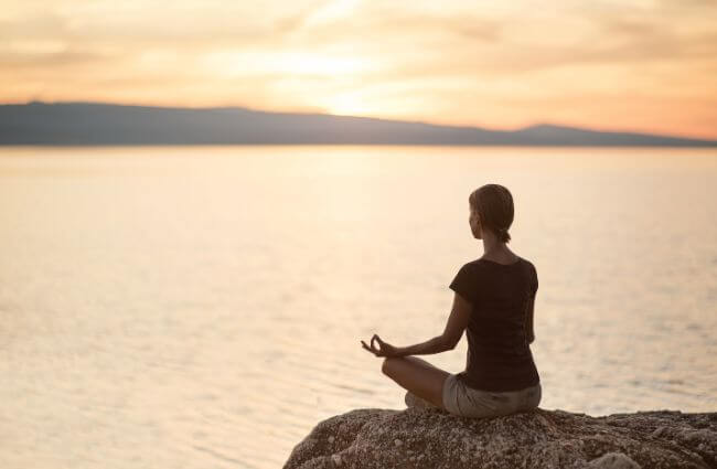 Meditation, Frau in meditativer Haltung im Sonnenuntergang am Meer